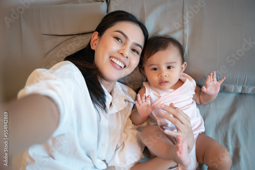 Happy mother and baby girl looking at camera making video call at home  family concept