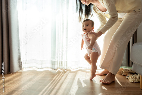 A baby girl learning first steps walk with mother, family, child, childhood and parenthood concept