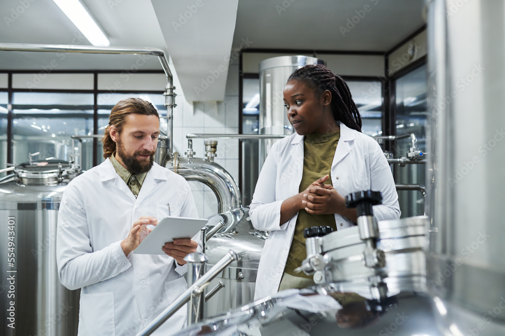 Obraz premium Brewery technologists using application on tablet computer when controlling work of equipment