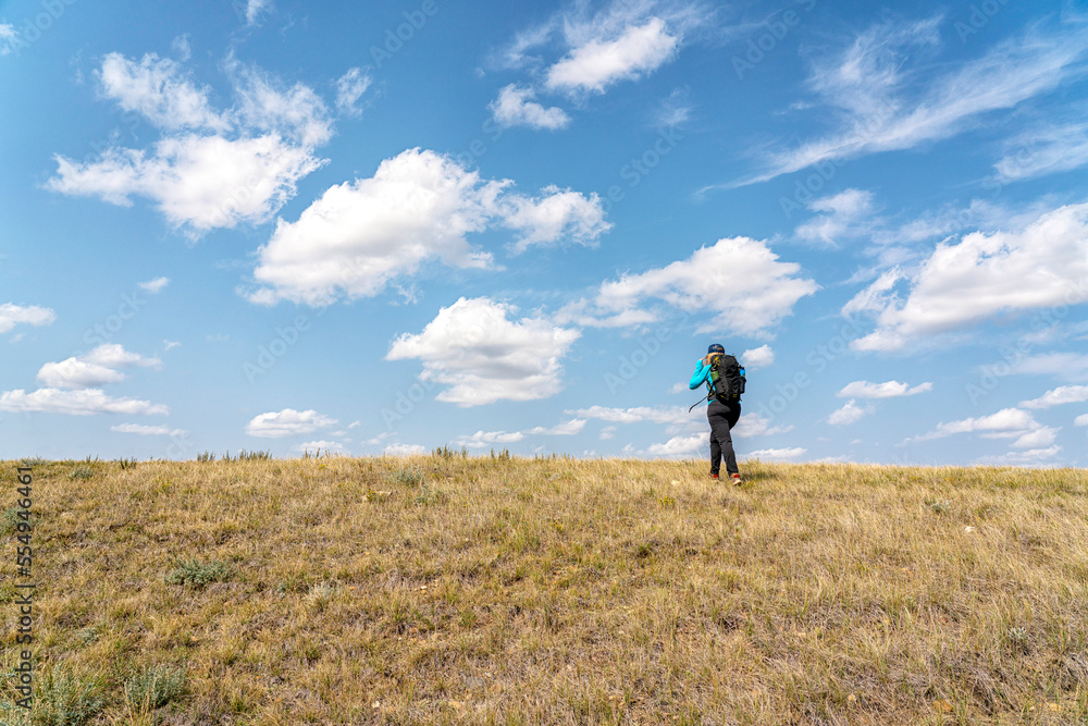 Woman walking towards the expansive sky whie hiking in rural Saskatchewan, Grasslands National Park; Saskatchewan, Canada Woman walking towards the expansive sky whie hiking in rural Saskatchewan, Grasslands National Park; Saskatchewan, Canada