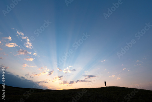 Silhouetted person watching the sunrise over the prairies in rural Saskatchewan, Grasslands National Park; Saskatchewan, Canada