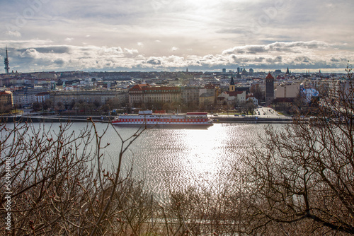 Vltava river - shining in sunbeams of winter sunrise with some ship next to shores and buildings in Prague