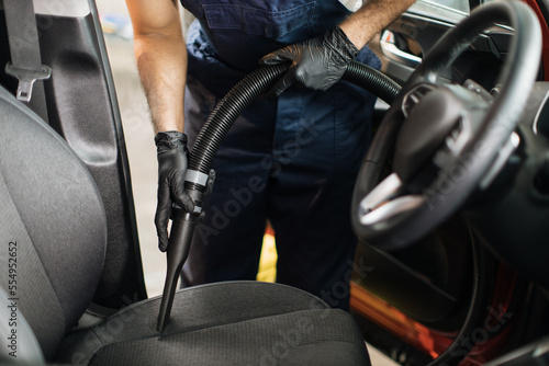 Closeup of hands of professional young male worker using vacuum cleaner for dirty car interior. Auto car service worker using vacuum cleaner to wash car seat. Details of car vacuum cleaning.