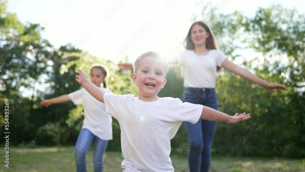 happy children run on grass with arms to sides. Cheerful children play plane pilot in park. Smile on children faces. Family on picnic in nature. Son and daughters play running on the grass in the park happy children run on grass with arms to sides. Cheerful children play plane pilot in park. Smile on children faces. Family on picnic in nature. Son and daughters play running on the grass in the park