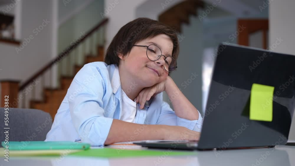 Tired schoolboy doing homework yawning falling asleep at table at home. Portrait of exhausted Caucasian boy sitting indoors surfing internet studying online Tired schoolboy doing homework yawning falling asleep at table at home. Portrait of exhausted Caucasian boy sitting indoors surfing internet studying online