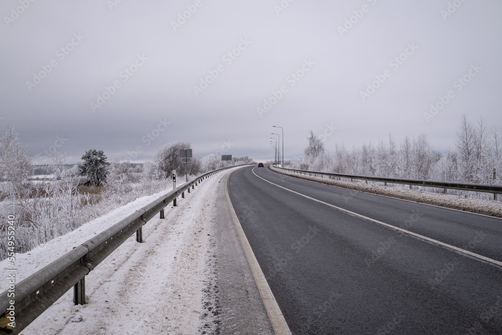 clean asphalt road Latvia landscape, winter time on Latvian highway, gloomy overcast day in December, safety railings