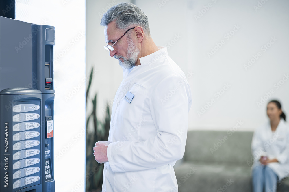 Fototapeta premium Gray-haired mature doctor standing near the slot machine