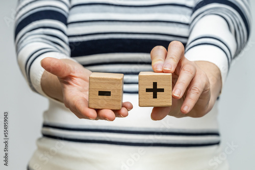 Pros and cons, A woman holds wooden blocks with a positive and negative symbol in her hands, the concept of pros and cons, ups and downs photo