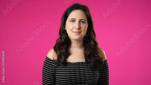 Smiling attractive brunette young woman 20s 30s years old posing isolated on pink background studio. People sincere emotions lifestyle concept. Looking at camera with charming smile © Robert Peak