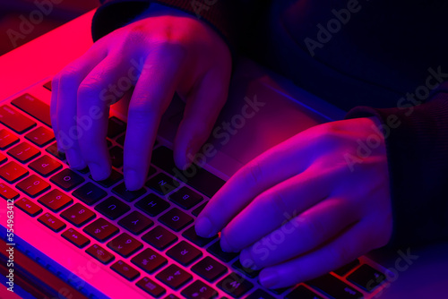 A man uses a laptop, close-up, male hands in neon lighting.