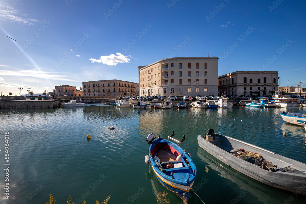 Fishing boats on water in the Ortigia island with the cityscape of Syracuse in Sicily, Italy