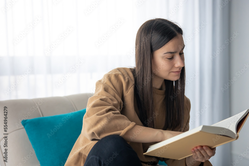 Attractive young woman is reading a book while sitting on the couch. Attractive young woman is reading a book while sitting on the couch.