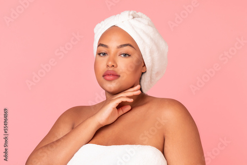 Attractive african american oversize lady with perfect skin posing wrapped in bath towel over pink studio background