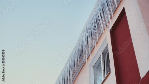 Large icicles hang from the overhang of the roof of the building. Falling ice- winter hazard for passersby