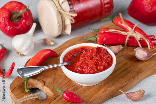 Traditional sauce adjika with hot chili pepper, paste harissa in white bowl on wooden board. Closeup