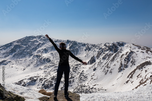 Rear view of woman on top of summit Kreiskogel spreading arms and looking at snowcapped mountain peak Zirbitzkogel, Seetal Alps, Styria, Austria, Europe. Hiking trail Central Alps in sunny winter © Chris