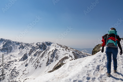 Rear view of woman with backpack hiking on snow covered hiking trail with panoramic view on snow capped mountain peak Zirbitzkogel and Kreiskogel, Seetal Alps, Styria (Steiermark), Austria, Europe