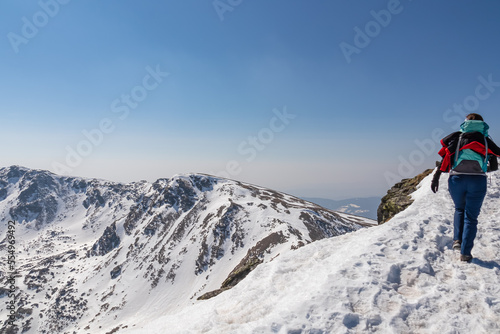 Rear view of woman with backpack hiking on snow covered hiking trail with panoramic view on snow capped mountain peak Zirbitzkogel and Kreiskogel, Seetal Alps, Styria (Steiermark), Austria, Europe
