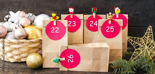 On a wooden background, paper bags fastened with clothespins with New Year's heroes, making an advent calendar.  Basket with Christmas decorations.  Front view.  Concept New Year and Christmas.