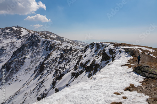 Rear view of woman with backpack hiking on snow covered hiking trail to radar station with scenic view on snow capped mountain peak Zirbitzkogel, Seetal Alps, Styria (Steiermark), Austria, Europe photo