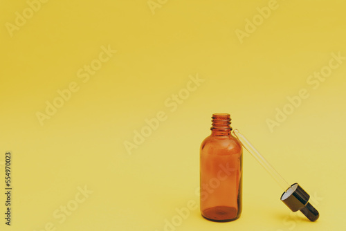 Facial serum in a glass brown bottle on a yellow background, cosmetics commercial shoot