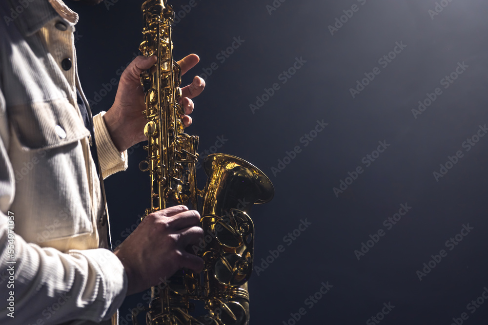 Obraz premium Saxophone in the hands of a man on a dark background, copy space.