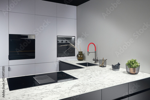 Upscale modern flat design loft kitchen with Induction cooker black glass hob with integrated hood or aspirating induction hob on marble light stoneware countertop panels with flower in vase and sink. photo