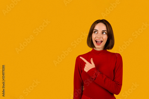 Cool excited young woman pointing at copy space on orange