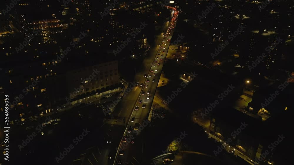 High angle view of stream of slowly moving cars on multilane road in urban borough. Tilt up reveal night cityscape with skyscrapers. New York City, USA High angle view of stream of slowly moving cars on multilane road in urban borough. Tilt up reveal night cityscape with skyscrapers. New York City, USA