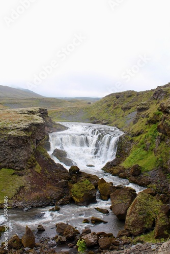 Majestic icelandic waterfall surrounded by green moss and grass with fresh glacier water. Icelandic weather. 
