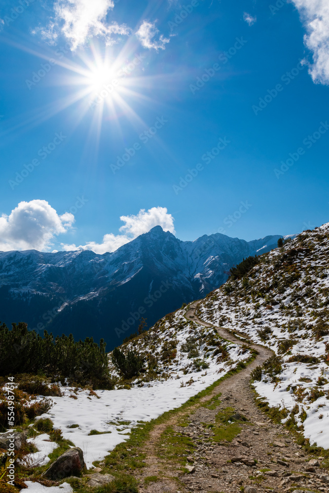During sunshine, a hiking path leads to a mountain massif (Vorarlberg, Austria)