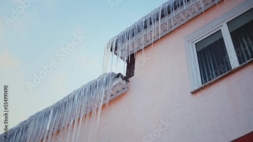 Large icicles hang from the overhang of the roof of the building. Falling ice- winter hazard for passersby
