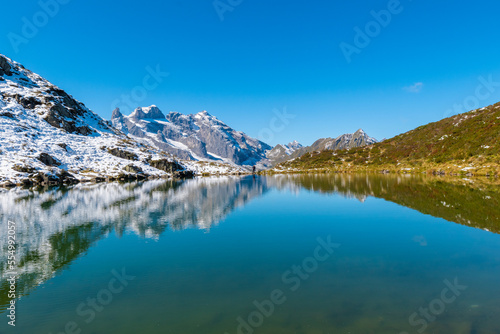 The clear tarn reflects the surrounding alpine panorama (Tobelsee, Vorarlberg, Austria)