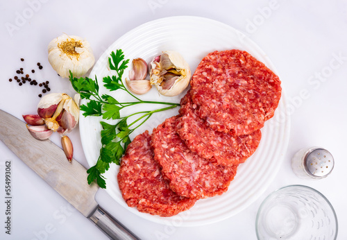 Plate of raw formed hamburger patties ready for cooking with fresh fragrant parsley, spicy garlic and allspice. Popular dish concept