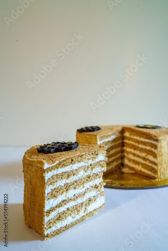 A slice of Russian Ukrainian Georgian honey cake with the whole cake in the background with a chocolate flourish on the top