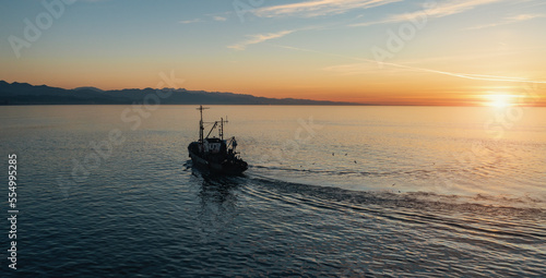 Fishing boat catching fish at sunset aerial view from drone. Small fishing trawler ship on sea surface. © DedMityay