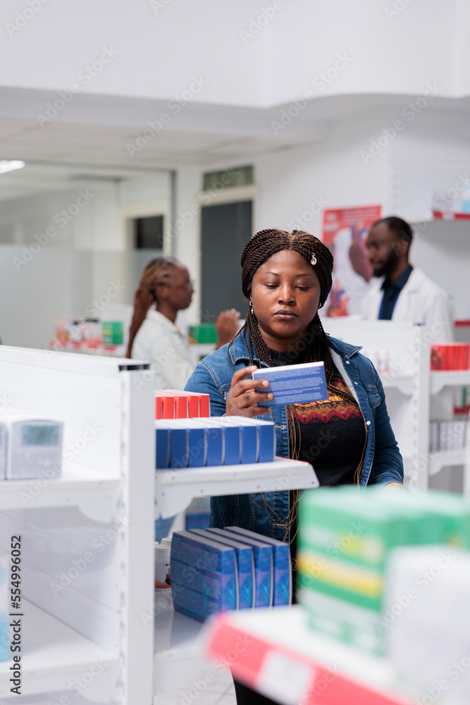 African american woman buying pills in pharmacy store, reading instruction, holding tablets package, standing near drugstore shelf. Client choosing medications, pharmaceutical business concept African american woman buying pills in pharmacy store, reading instruction, holding tablets package, standing near drugstore shelf. Client choosing medications, pharmaceutical business concept