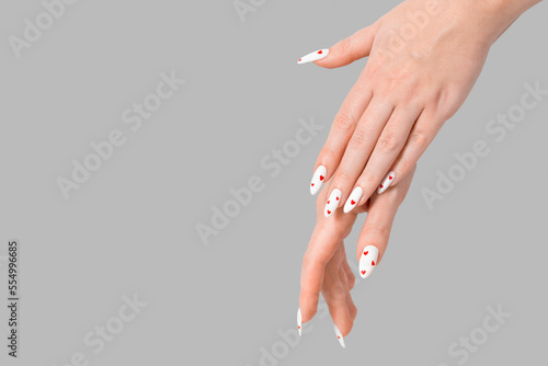 Female manicure two hands minimal gel polish white long nails and red hearts desing gray isolated background. Beauty spa  Valentine s Day  love concept