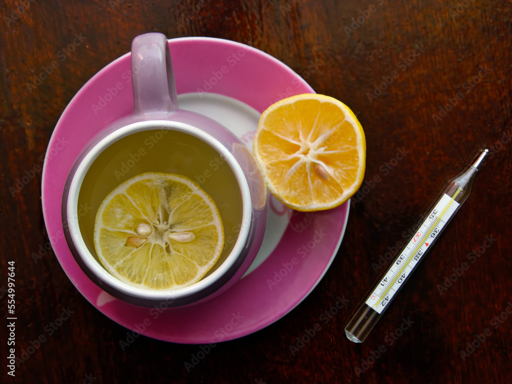 a thermometer, a cup of hot tea with lemon for a cold on a wooden background. the concept of prevention and treatment of cold diseases a thermometer, a cup of hot tea with lemon for a cold on a wooden background. the concept of prevention and treatment of cold diseases