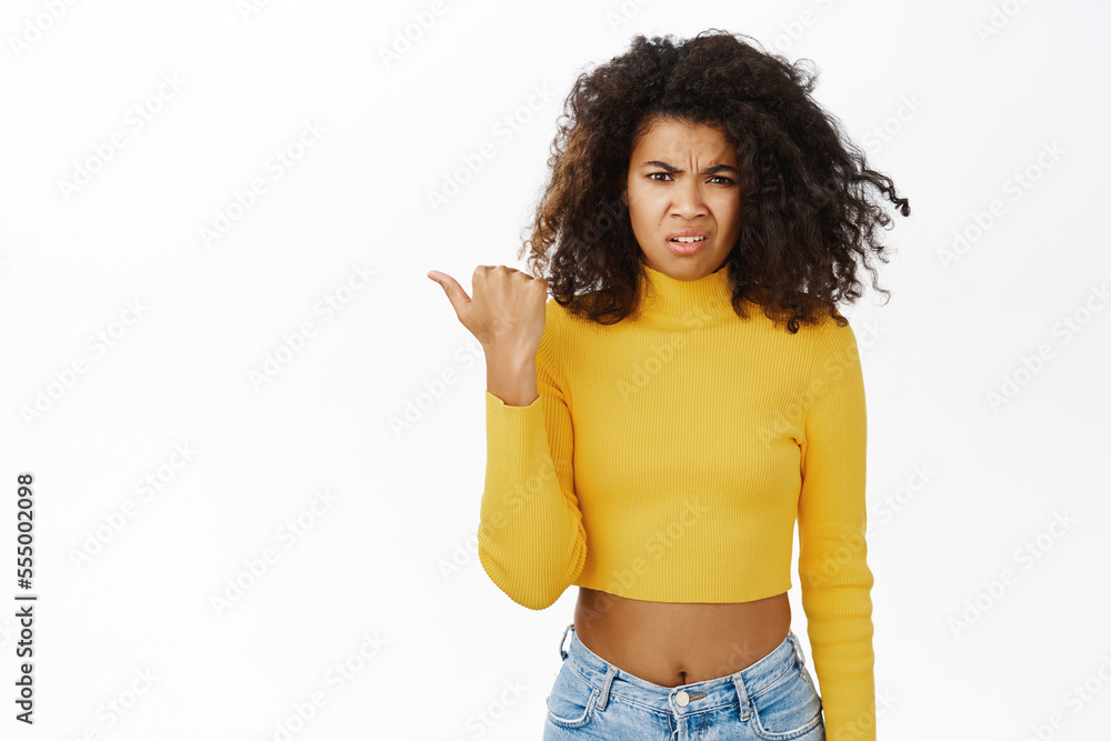 Confused, disappointed african american woman, pointing left, grimacing from dislike, disapprove smth, standing over white background Confused, disappointed african american woman, pointing left, grimacing from dislike, disapprove smth, standing over white background