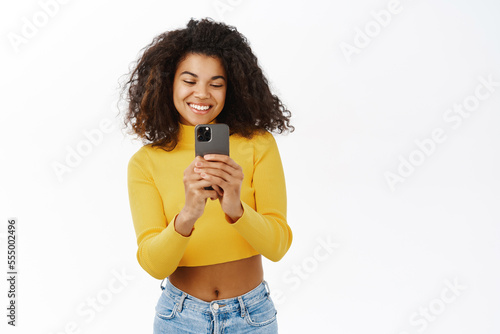 Portrait of beautiful teen girl smiling, taking pictures, photos on smartphone, pointing at smth while recording video on mobile phone