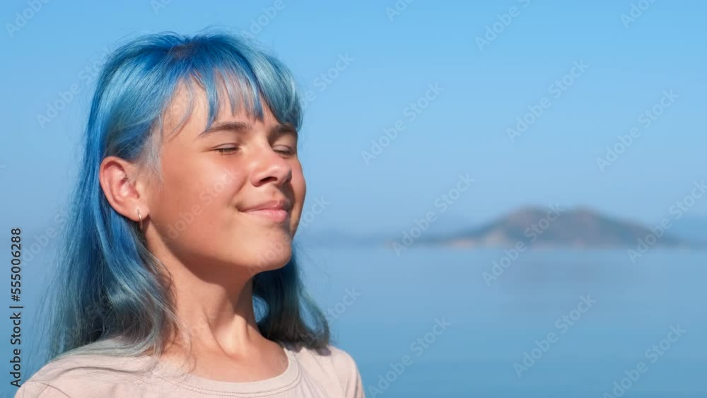 Joyful teen enjoy wind on shore. A playful young girl with blue hair enjoy the turquoise ocean from the beach under summer sun. Joyful teen enjoy wind on shore. A playful young girl with blue hair enjoy the turquoise ocean from the beach under summer sun.