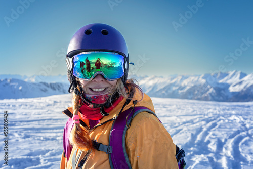 portrait of young woman in a bright jacket and blue helmet with a bright ski mask with reflection of winter ski resort