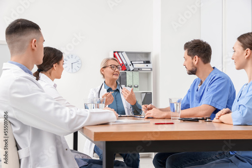 Medical conference. Team of doctors having discussion with speaker at wooden table in clinic