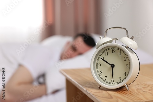 Man sleeping in bedroom, focus on alarm clock. Space for text