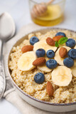 Bowl of delicious cooked quinoa with almonds, bananas and blueberries on white table, closeup