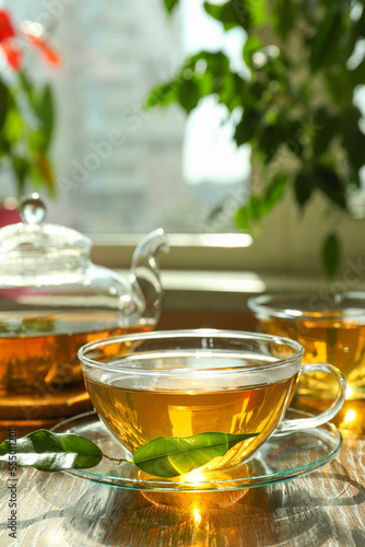 Fresh green tea in glass cups, leaves and teapot on wooden table