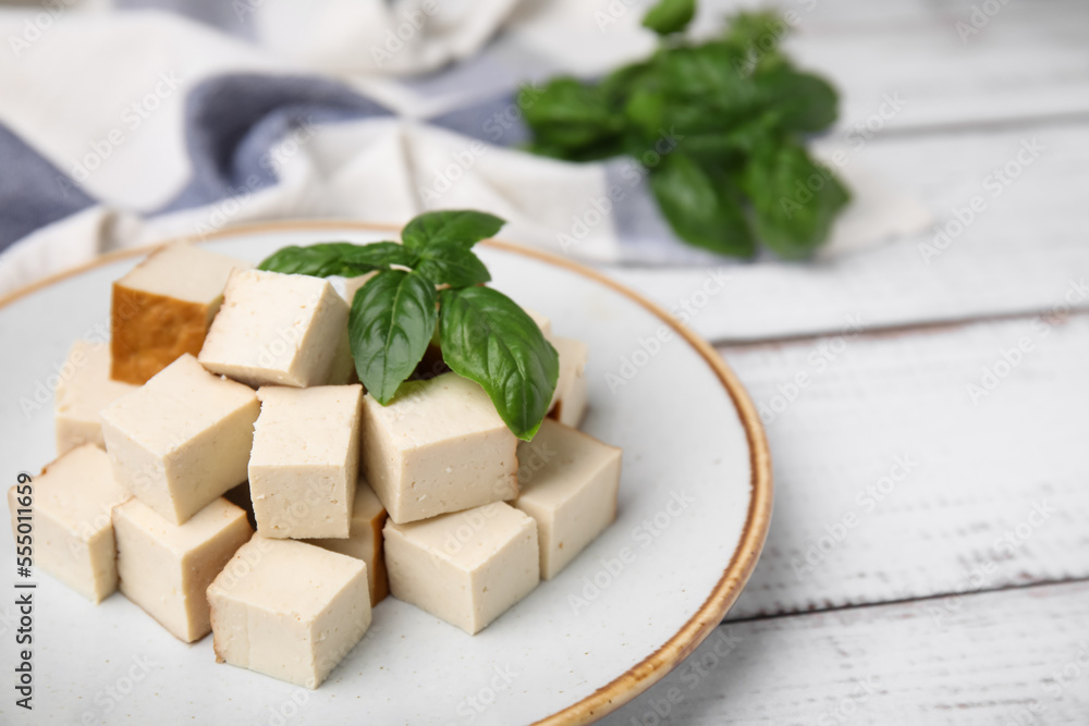 Plate with delicious smoked tofu and basil on white wooden table, closeup