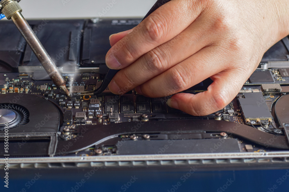 computer technician A laptop motherboard repairman is using lead solder to repair some ICs for his desk. fix motherboard computer technician A laptop motherboard repairman is using lead solder to repair some ICs for his desk. fix motherboard
