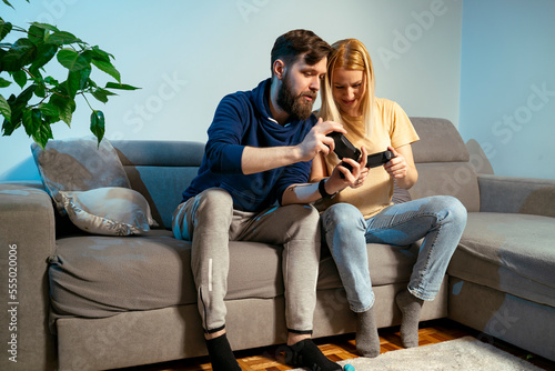 Young couple man and woman, playing video games at home, guy showing girl controls 